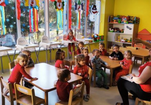 Dzieci siedzące przy stole opisują obrazki pokazywane przez opiekunkę.
